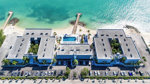An aerial view of a hotel with a pool, parking, and a beach.