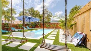 Un patio trasero con piscina, dos columpios, sillas de descanso y una valla de madera.