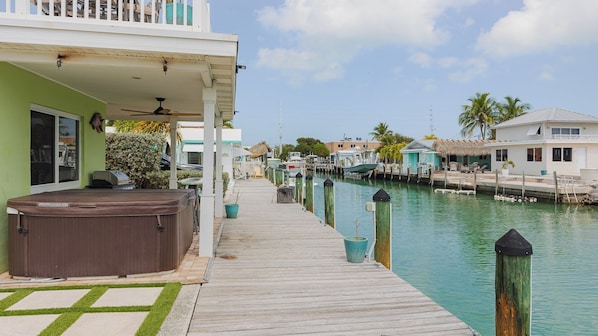 A waterfront property with a wooden dock, a hot tub, and a covered patio.