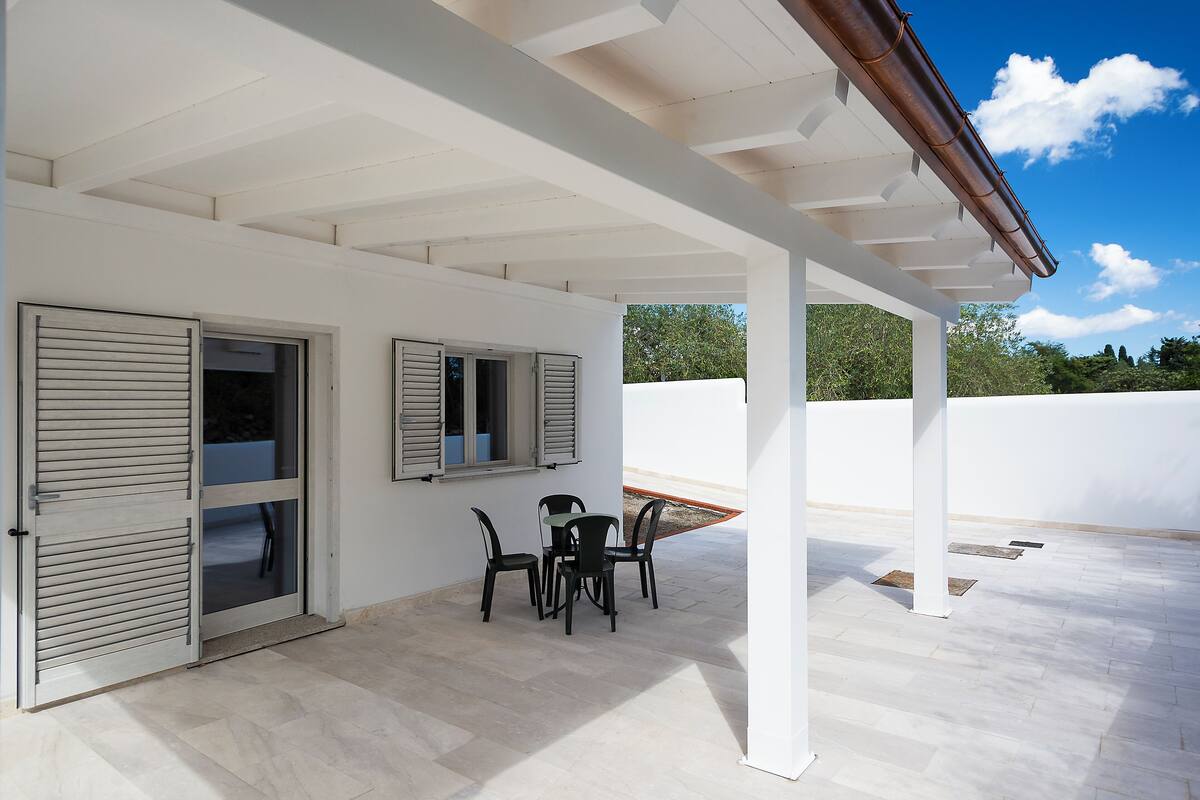 An outdoor patio with a table and chairs, white walls, and a pergola.