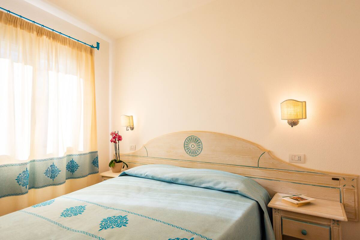 A hotel room with a bed, a nightstand, a lamp, and a window with curtains.