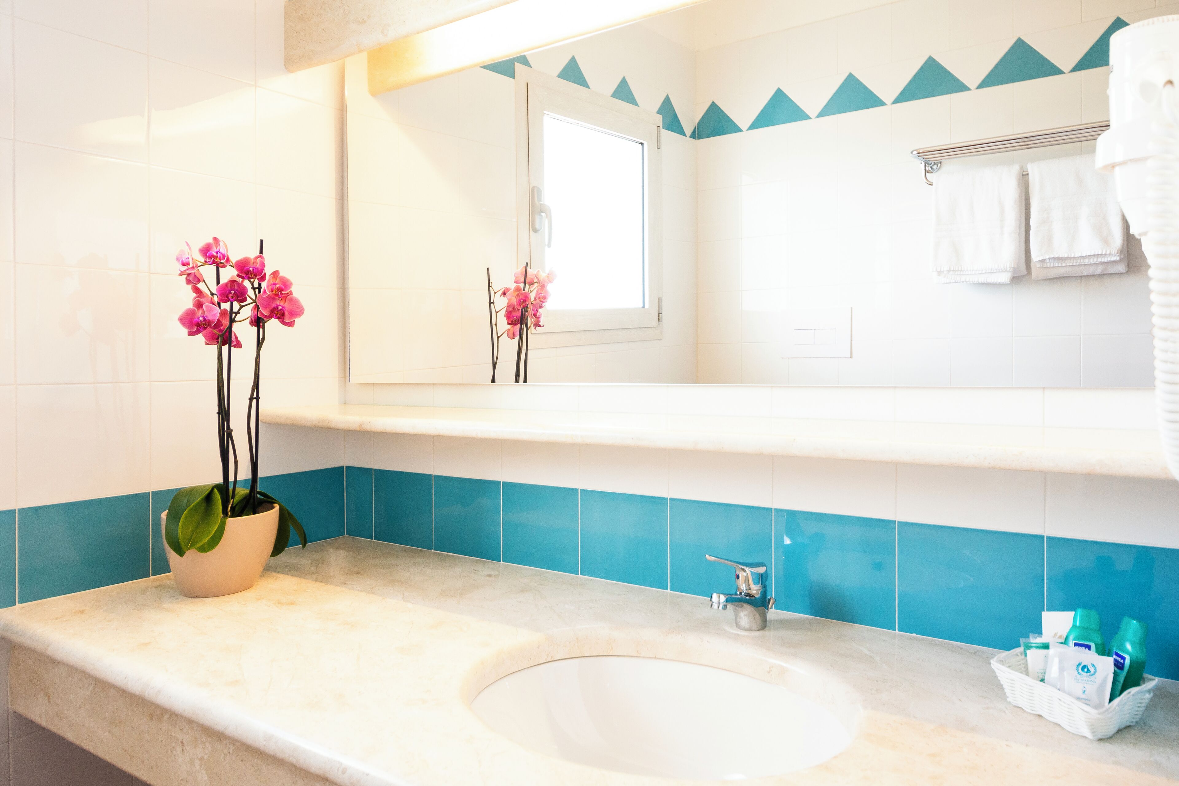 Ein Badezimmer mit Waschbecken, Spiegel, Orchidee im Topf und Handtuchhalter.