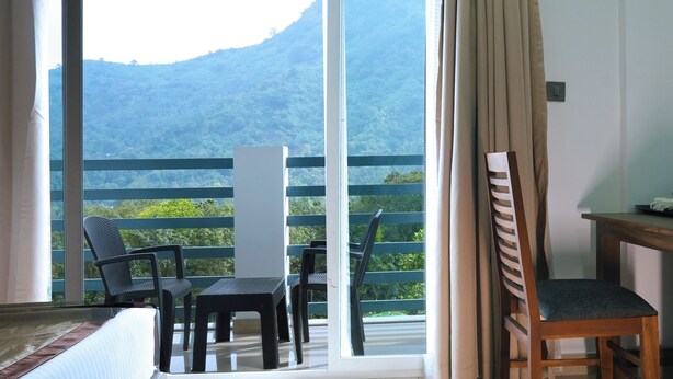 Habitación con balcón que da a un paisaje montañoso. Hay dos sillas y una mesa en el balcón.