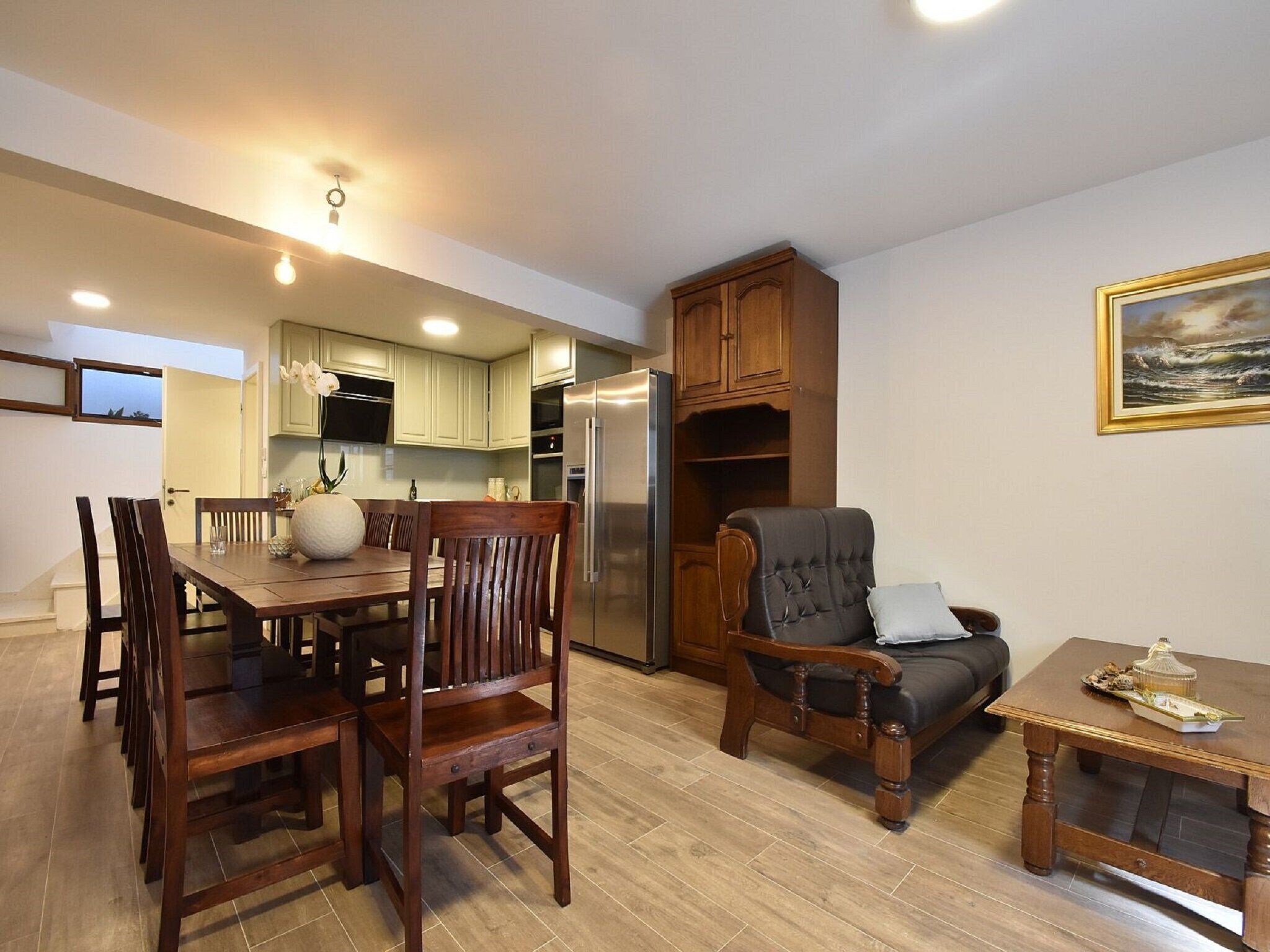 A dining area with wooden chairs and a table, a sofa, and a small table with decorative items.