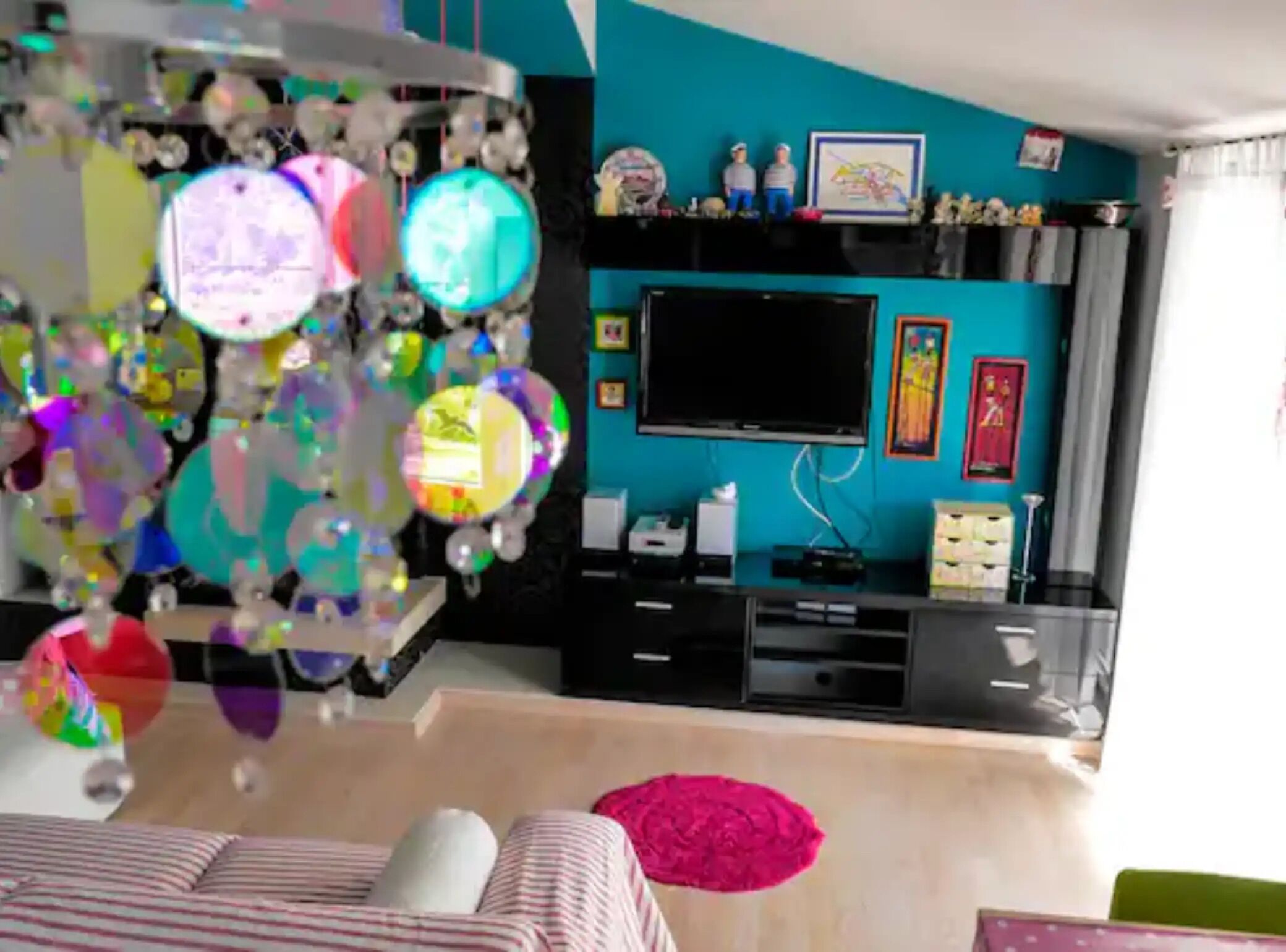 Quarto com parede verde-água, televisão de tela plana, unidade de entretenimento preta e decoração no teto com detalhes refletivos.