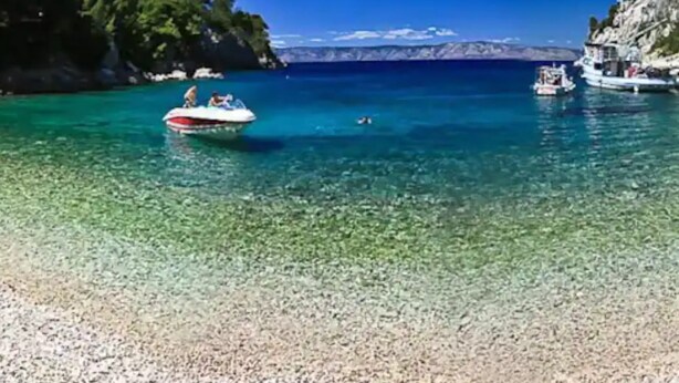 A clear turquoise sea with boats, rocky cliffs, and a pebble beach. - House of Green Experience (Omis)