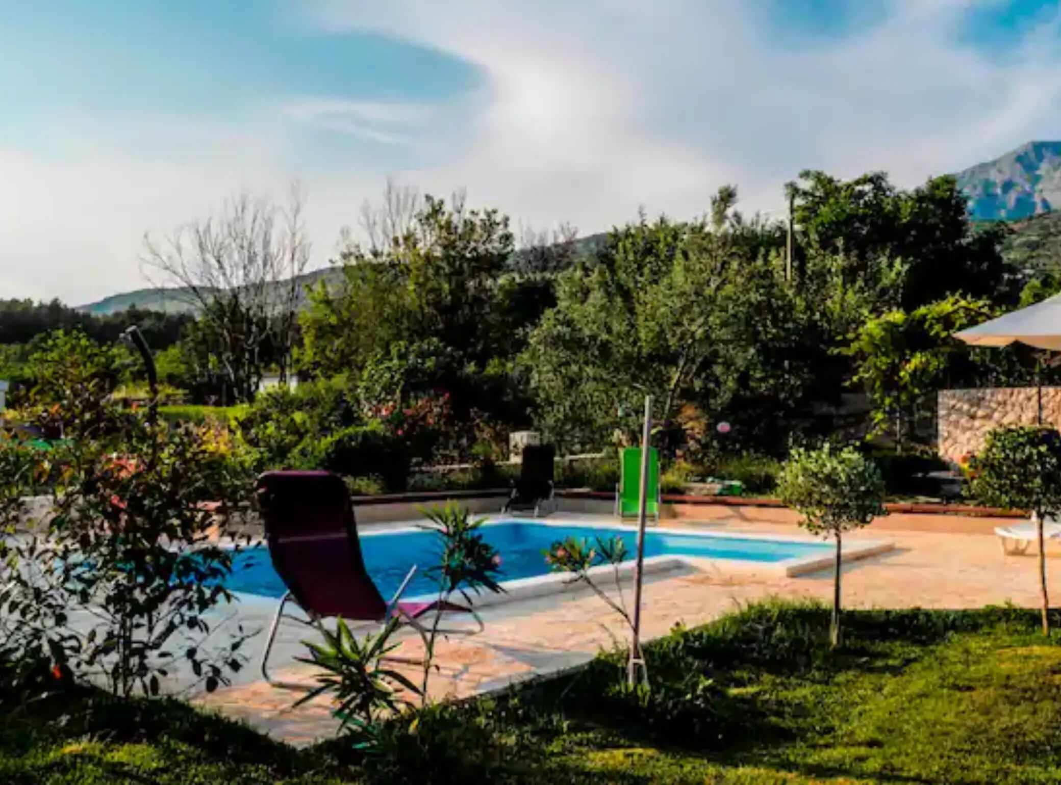A swimming pool with a red lounge chair, surrounded by greenery and a stone wall.