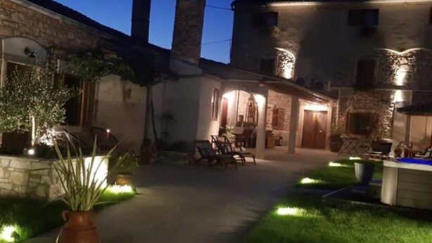 A stone building with a patio area, outdoor seating, and a well-lit garden. - Charming Rooms & Apartments Stelio (Marcana)