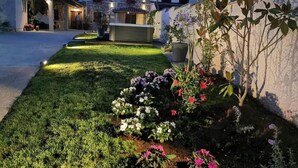 A well-maintained garden with a variety of flowers and a neatly trimmed lawn in front of a building with stone walls and a tiled roof. - Charming Rooms & Apartments Stelio (Marcana)