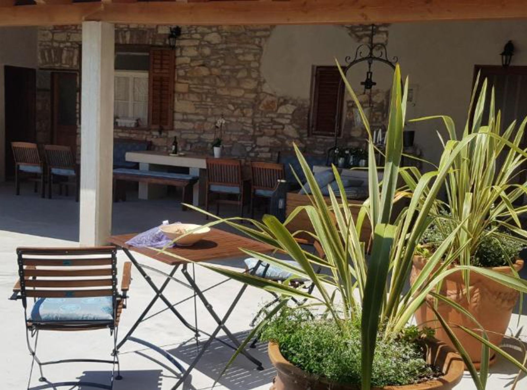 An outdoor patio with a wooden table, chairs, and potted plants.