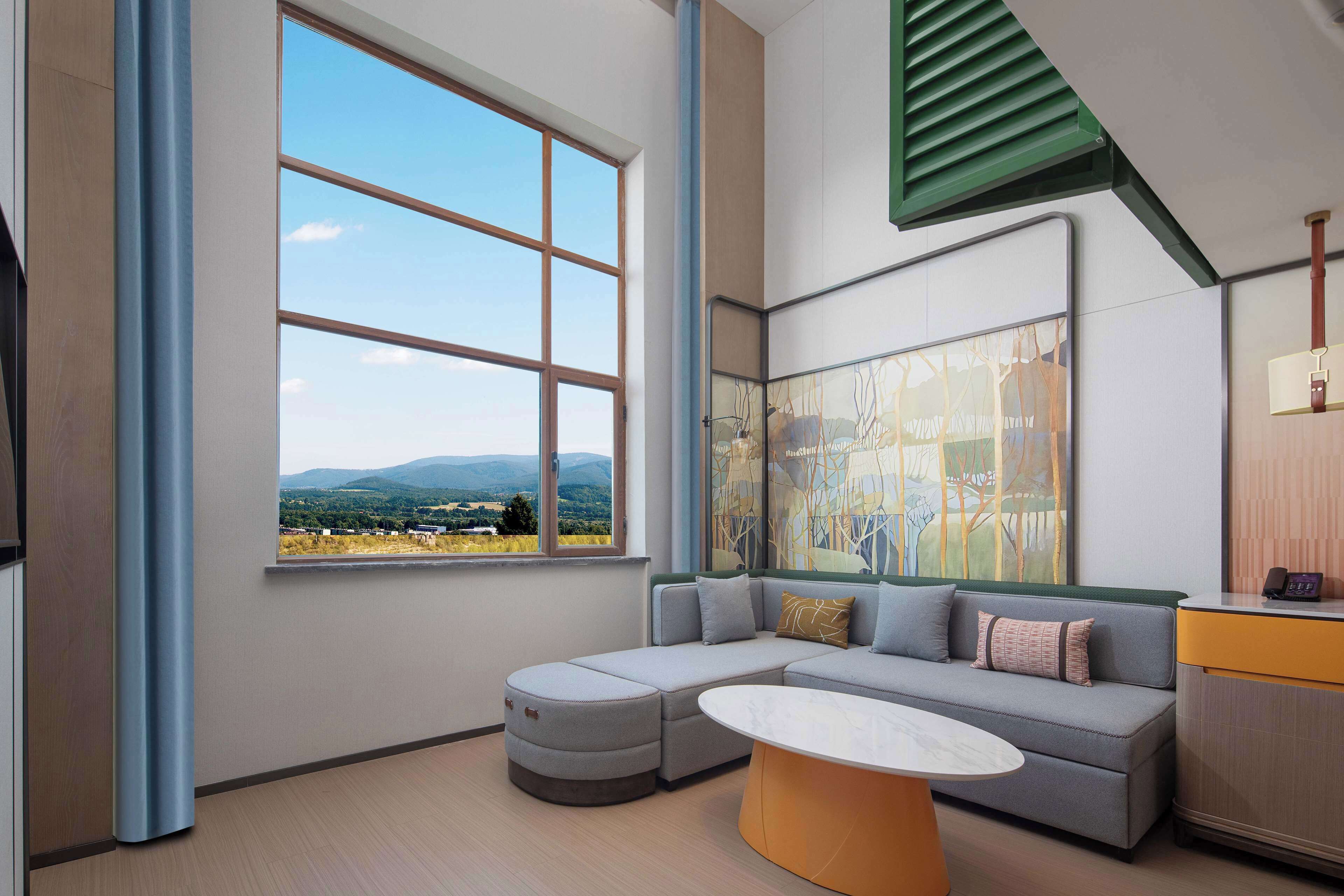 A modern living room with a large window, a sectional sofa, a coffee table, and a desk with a telephone.