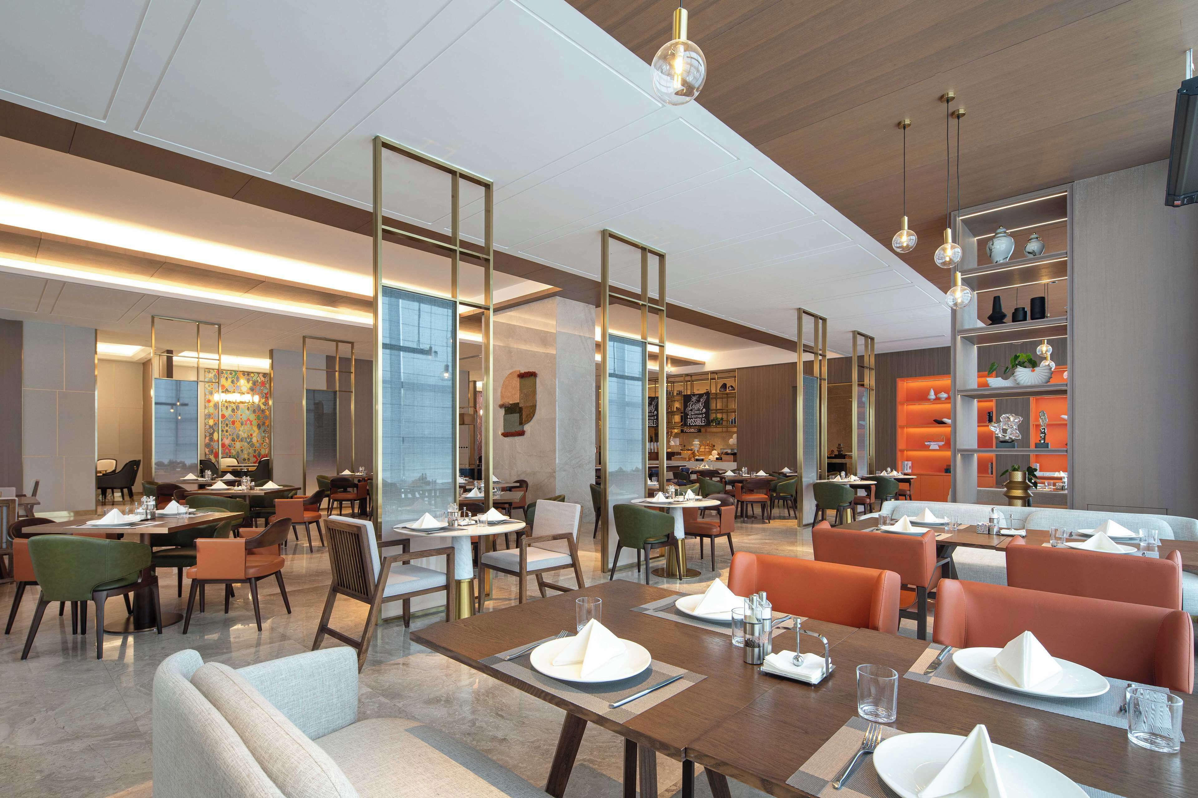 Un restaurant spacieux doté de plusieurs espaces de restauration, d’un décor moderne et offrant une variété de types de sièges.
