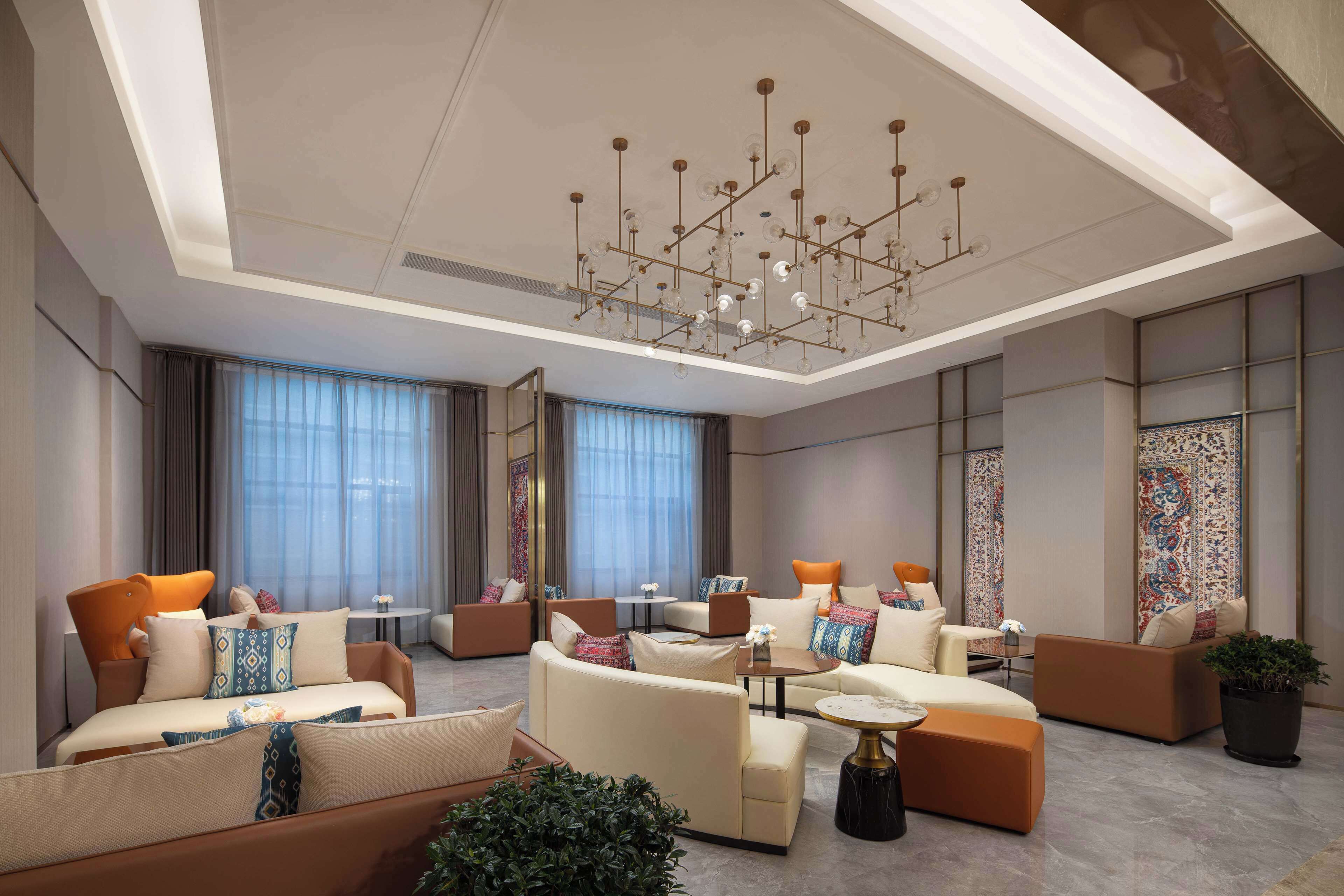 A modern hotel lobby with a central seating area, a chandelier, and large windows.