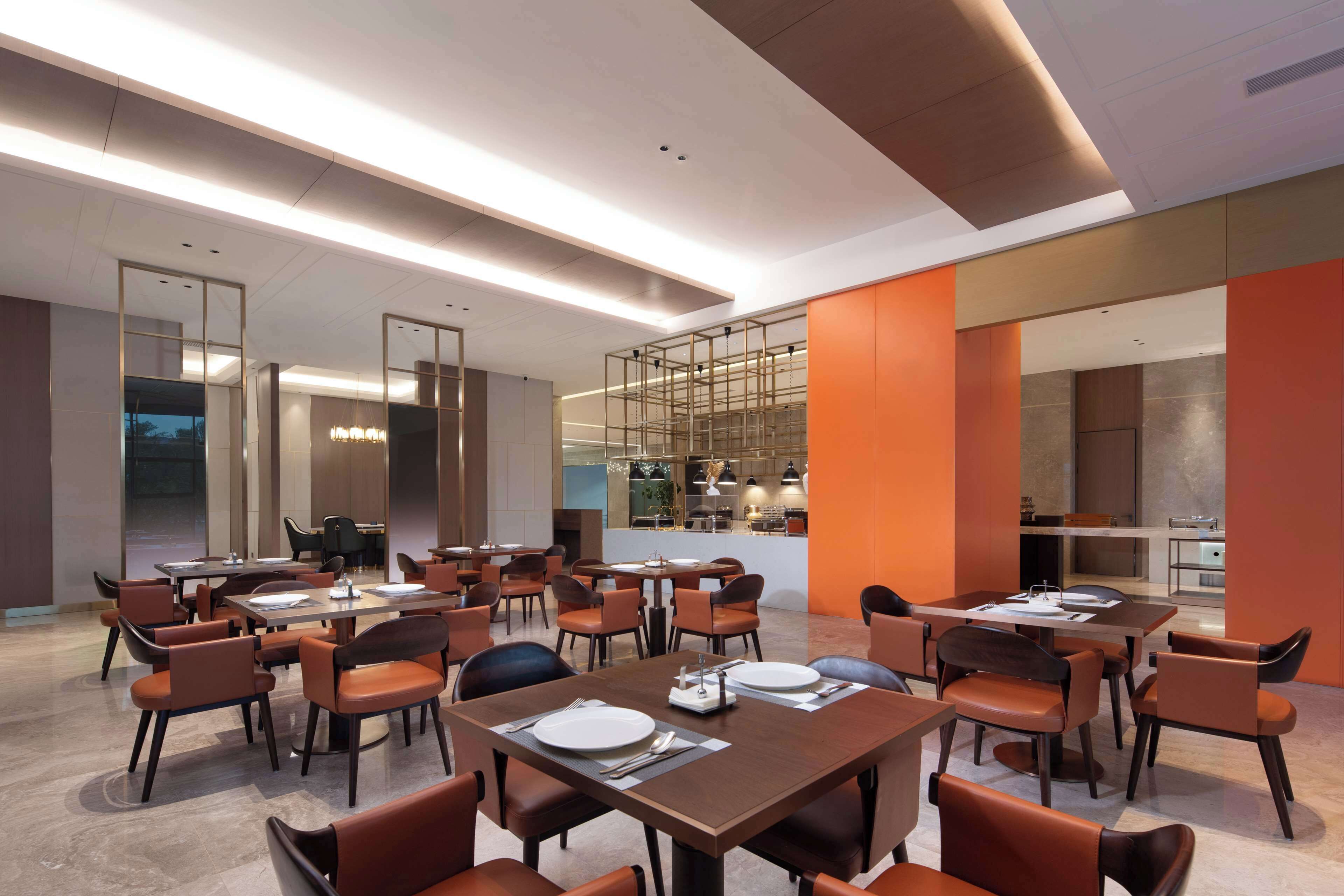 A modern dining area with multiple tables and chairs, a kitchen in the background, and a bright, well-lit ambiance.