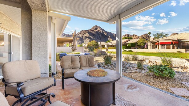 A covered patio with a round table and two chairs, a mountain view, and a well-maintained garden.