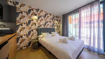 Una habitación de hotel con cama, escritorio, silla y ventana con cortinas.