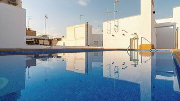 Une piscine d’un bleu éclatant, bordée de carreaux, entourée de murs blancs et de balcons ornés de diverses antennes et de caméras de surveillance.