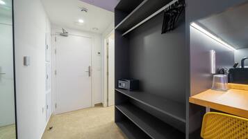 A modern hotel room with a minimalist design, featuring a wooden desk, a chair, a built-in shelf, and a door leading to another room.