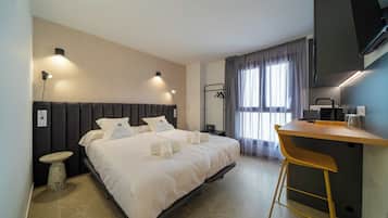 Una habitación de hotel con una cama, mesita de noche y un pequeño taburete.