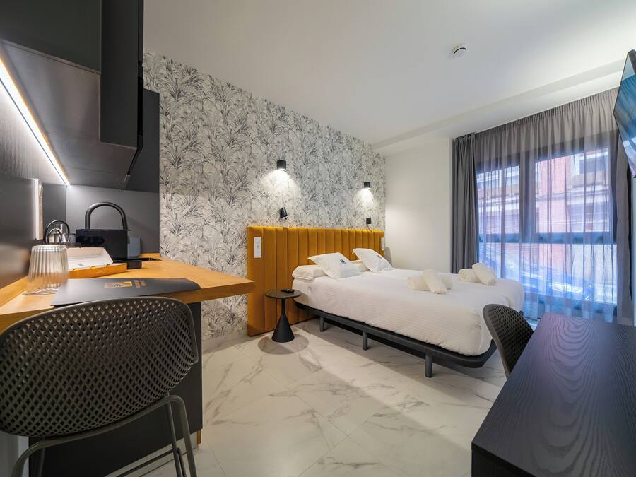 A modern hotel room with a bed, desk, chair, and a TV mounted on the wall.