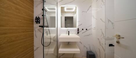 A modern bathroom with a glass-enclosed shower, a white sink with a mirror above it, and a wooden wall on one side.