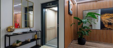 Una moderna zona de recepción con un panel de madera, un espejo grande, un globo terráqueo sobre una mesa consola y una planta en maceta.