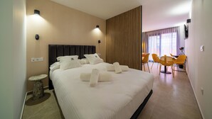 A hotel room with a large bed, a small round table, a desk with chairs, and a view of the outdoors through a window. - Alicante Smart (Alicante)