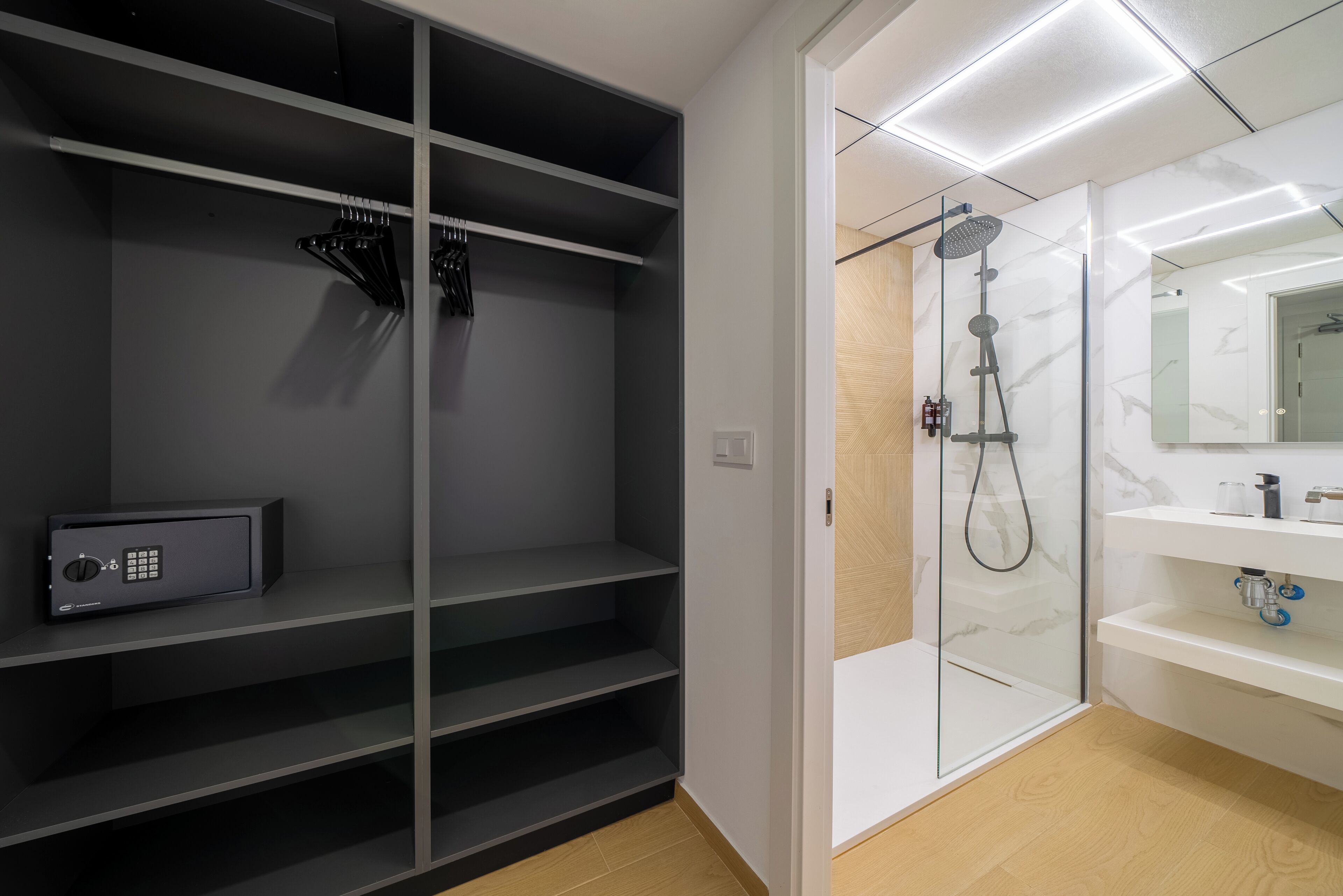 A modern bathroom with a walk-in shower, a built-in safe, and a vanity with a mirror.