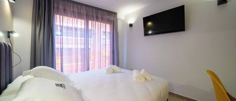Una habitación de hotel con una cama, un televisor montado en la pared y una silla.