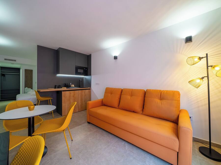 A modern living room with a sofa, yellow chairs, a dining table, and a kitchen area.