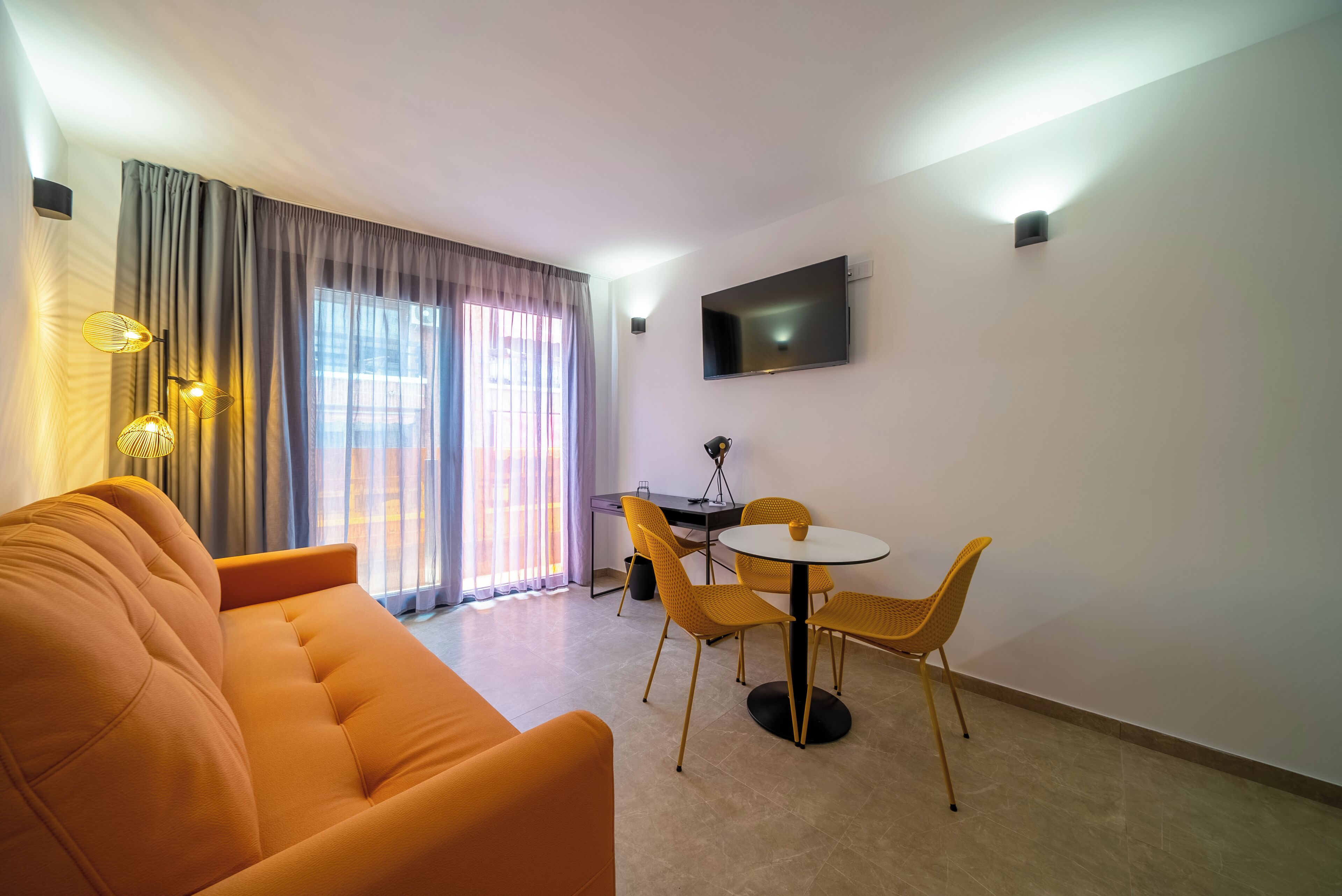 Un salon moderne comprenant un canapé, une table à manger, des chaises et un téléviseur fixé au mur.