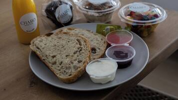 Een ontbijtkarretje met brood, yoghurt en fruit op een houten tafel in een hotelkamer.