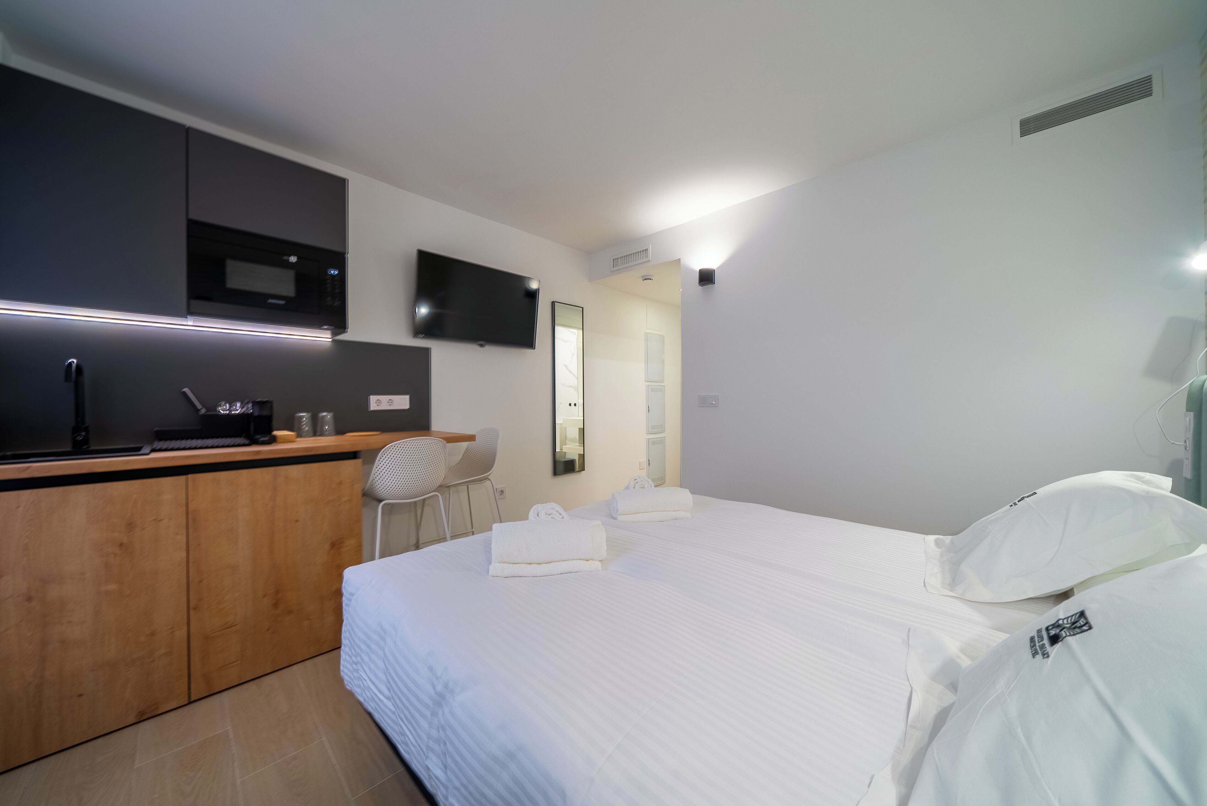 Una camera d'albergo moderna con un letto, una scrivania con televisore a schermo piatto, un forno a microonde e una sedia.