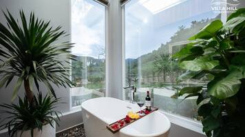 Un baño moderno con una bañera independiente, una ducha con mampara de vidrio y un amplio ventanal con vistas al paisaje circundante.