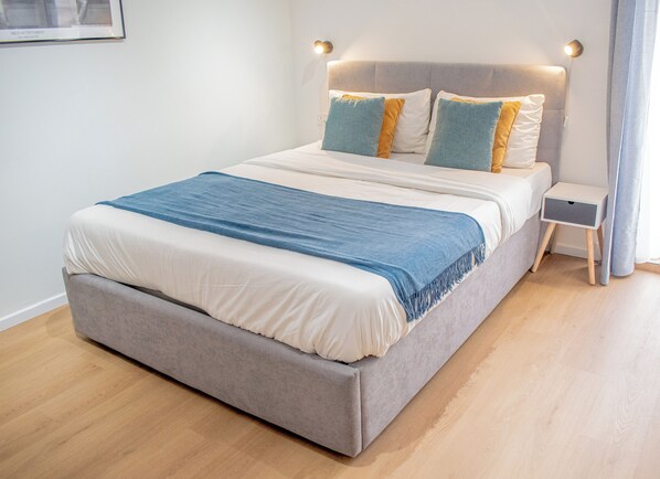 A neatly made bed with a blue throw blanket, a grey upholstered headboard, and bedside tables with lamps.