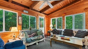 A cozy cabin interior with wooden walls, large windows, and a central seating area with a coffee table. - Unusual Latitude Limit 7 3 Bedroom Villa (Raymond)