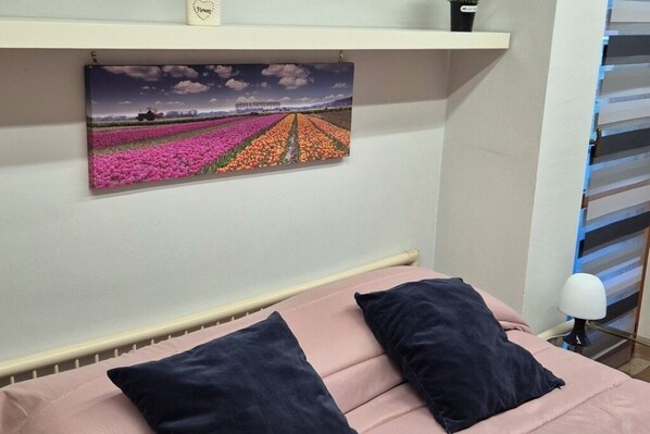 A bedroom with a bed, pillows, a nightstand, and a wall-mounted picture of a tulip field.