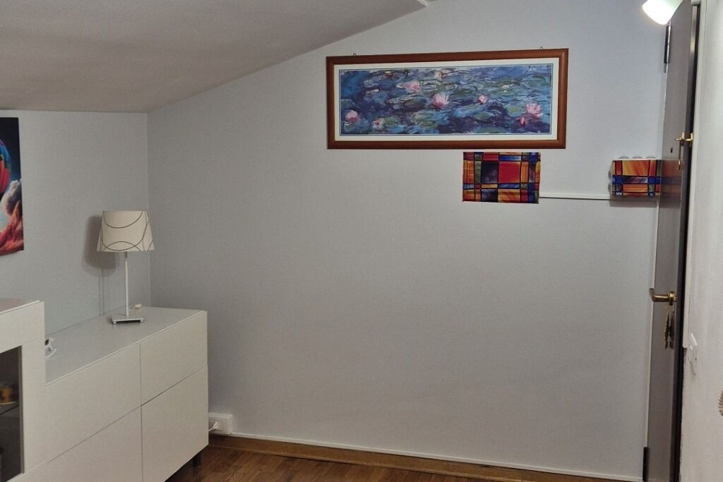 Une pièce avec une armoire blanche, un tableau encadré et une petite œuvre d’art colorée accrochée au mur.
