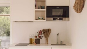 A modern kitchen with white cabinetry, a Bosch microwave, and a sink. - Casas de Arroz - Cabin (Possanco - Comporta)