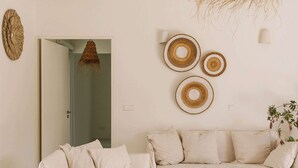 A minimalist living room with a white sofa, a woven wall hanging, and a fruit bowl on the table. - Casas de Arroz - House (Possanco - Comporta)