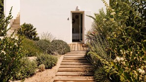 A pathway leading to a white building with a door and a small porch area.