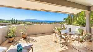 A balcony with a table and chairs, potted plants, and a view of the sea and mountains.