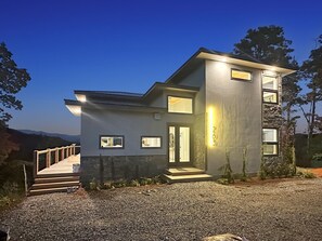 Uma casa moderna de dois andares com entrada por uma escadaria de madeira e acesso por uma entrada de cascalho.