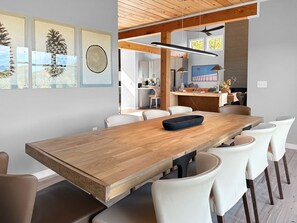 Uma área de jantar moderna com mesa de madeira, cadeiras brancas e luminária pendente.
