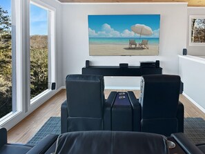 Ein Zimmer mit großem Fenster, einem Strandbild und einer Sitzecke mit Stühlen und Tisch.