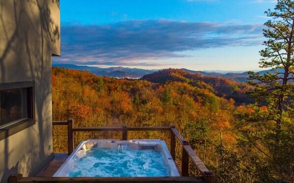 Un jacuzzi en una terraza de madera con vista a una cadena montañosa boscosa.