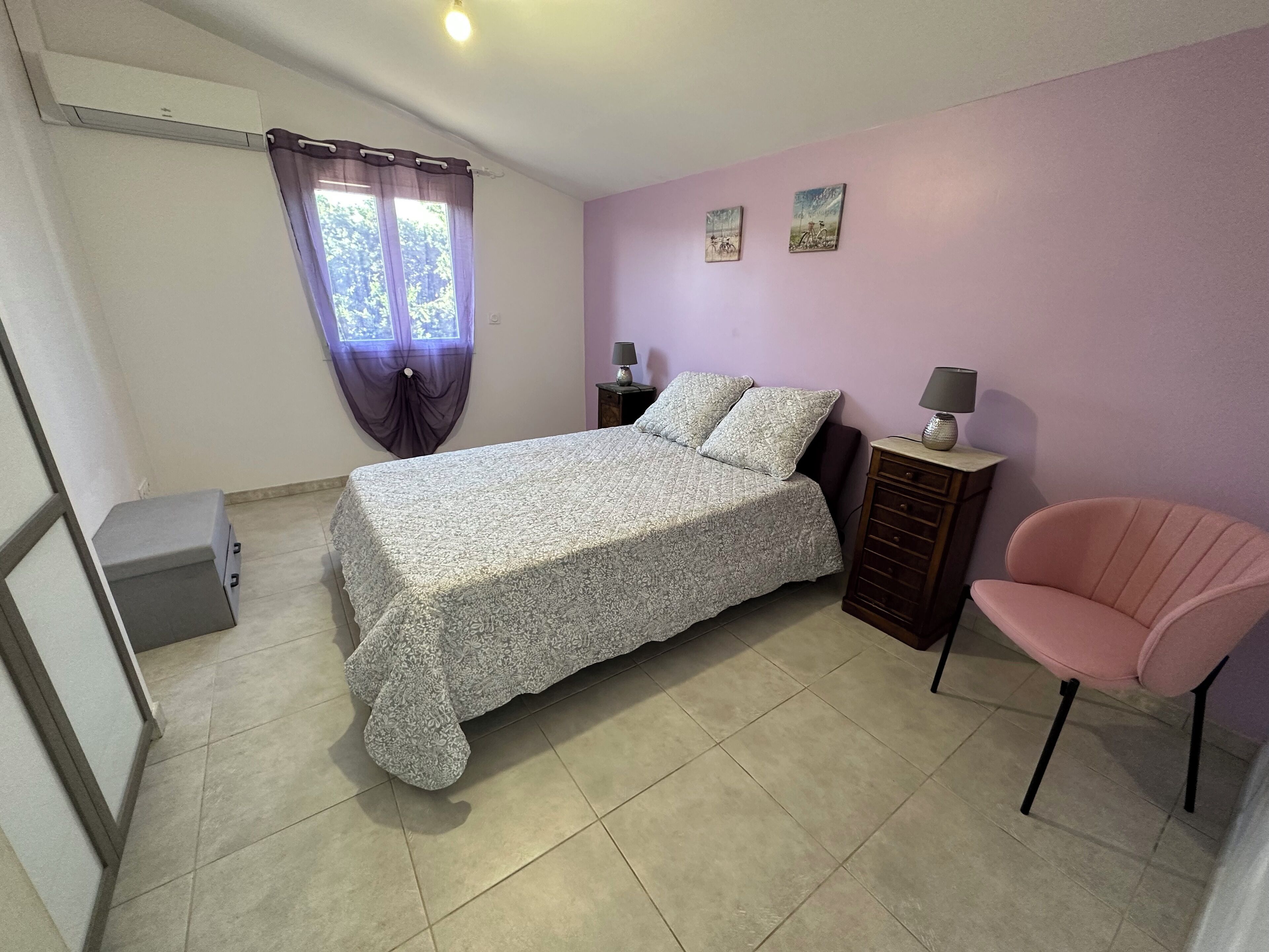 Une chambre à coucher comprenant un lit, une chaise, une table de chevet et un petit meuble.