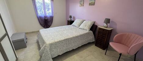 A bedroom with a bed, a chair, a nightstand, and a small cabinet.