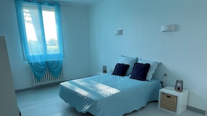 Une chambre à coucher avec un lit, une table de chevet, une lampe et une fenêtre avec des rideaux.