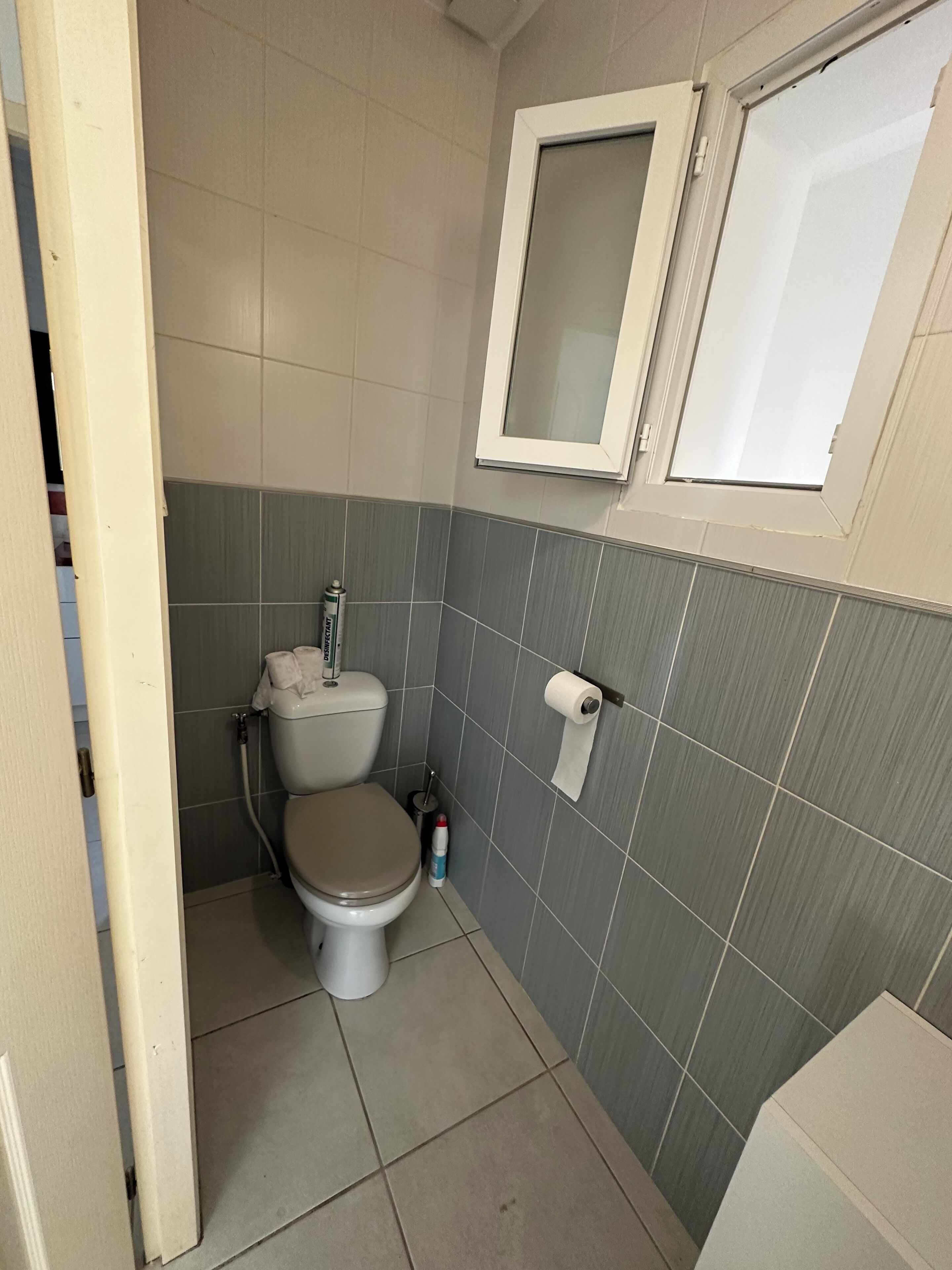 A small, compact bathroom with a toilet, a towel dispenser, and a toilet paper holder on the wall.